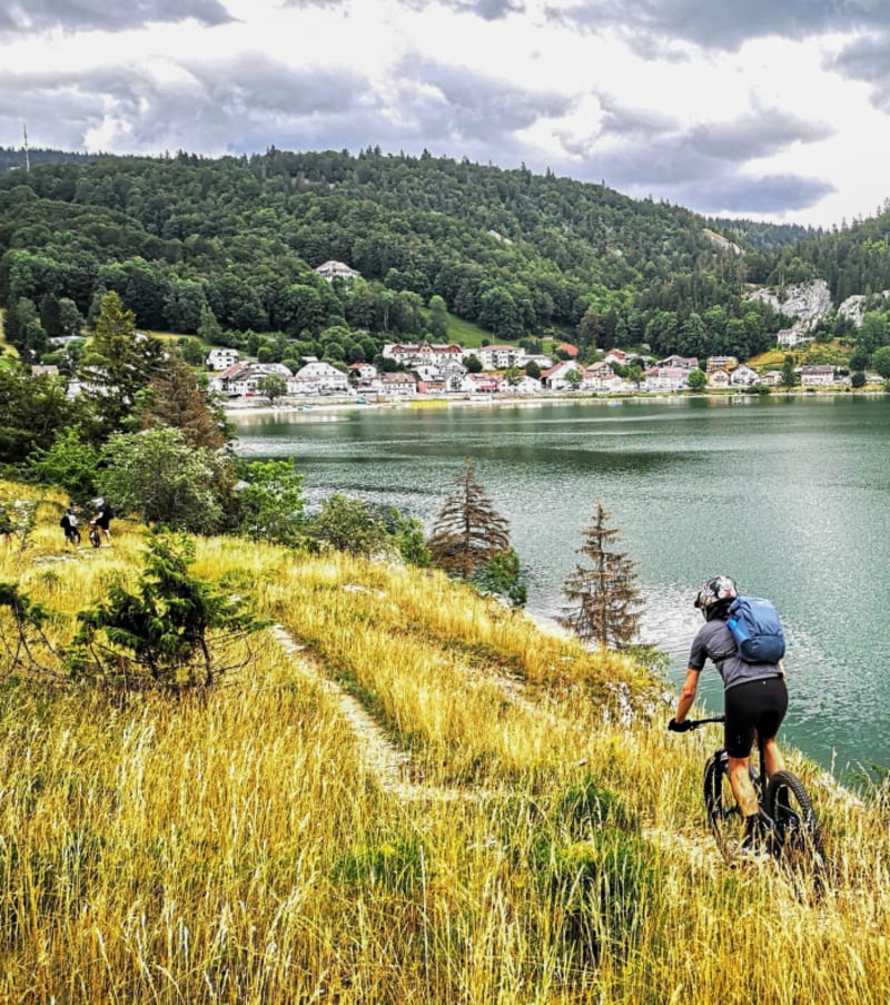 VTTiste en itinérance sur les crêtes du Jura Suisse surplombant un lac alpin et des montagnes boisées