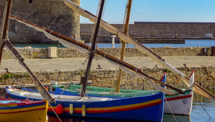 Bateaux traditionnels colorés dans le port de Collioure avec église et fortifications médiévales en arrière-plan