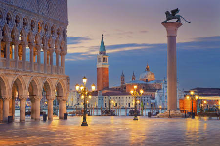 Vue de la Place Saint-Marc à Venise à l'aube, avec la colonne du Lion de Saint-Marc à droite, le palais des Doges à gauche, et le campanile de l'île San Giorgio Maggiore en arrière-plan, illuminant doucement la scène sous un ciel pastel.
