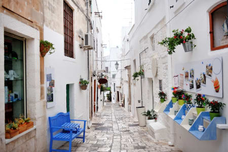 Charmante ruelle étroite d’Ostuni, en Italie, bordée de maisons blanchies à la chaux, de pots de fleurs colorés et de petites boutiques locales