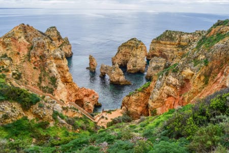 Vue plongeante sur Ponta da Piedade, un site emblématique de l'Algarve, au Portugal, avec ses formations rocheuses dorées sculptées par l'océan et un escalier descendant jusqu'à l'océan