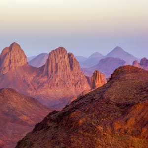 Paysage spectaculaire des montagnes du Hoggar en Algérie, baignées d'une lumière douce et rosée du crépuscule, mettant en valeur leurs formations rocheuses majestueuses