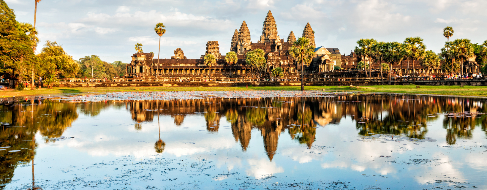 Vue emblématique du temple d'Angkor Wat au Cambodge, entouré de palmiers, avec son reflet parfaitement capturé dans les eaux calmes d'un bassin