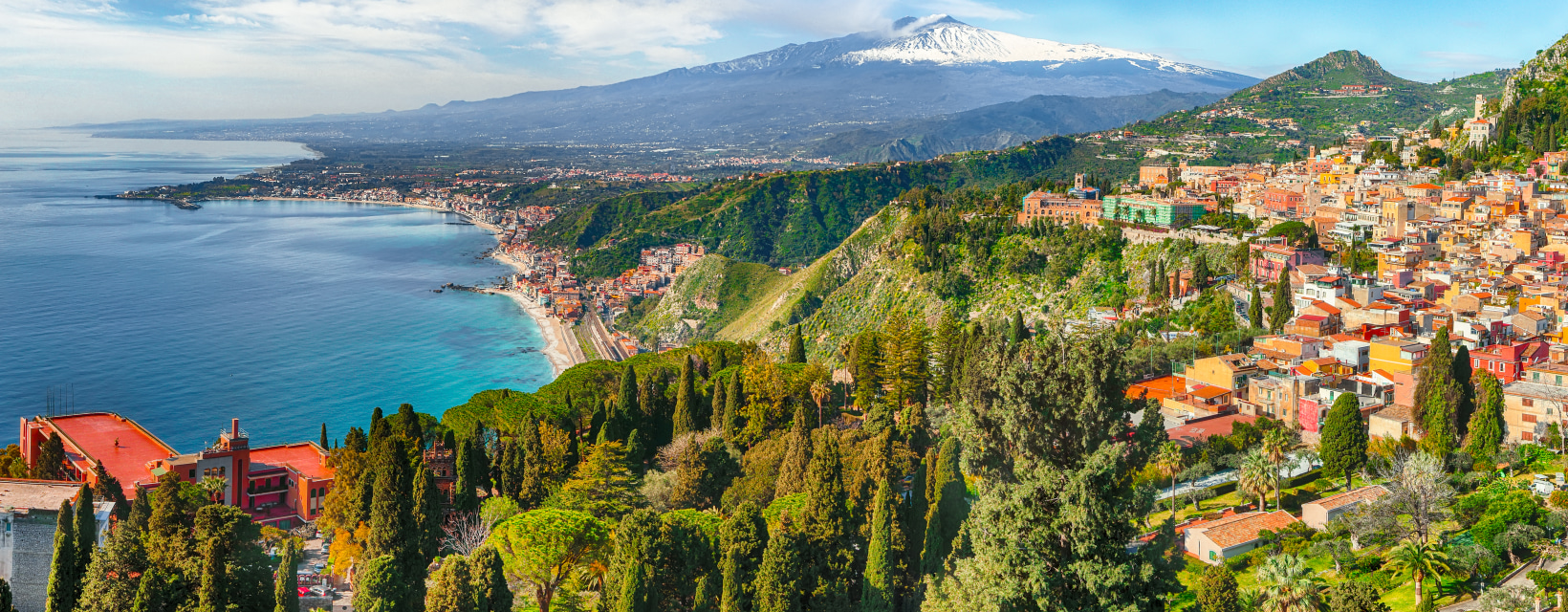 Paysage spectaculaire de la côte sicilienne, avec une mer turquoise, des collines verdoyantes et un village pittoresque. En arrière-plan, le majestueux mont Etna, enneigé, domine l'horizon