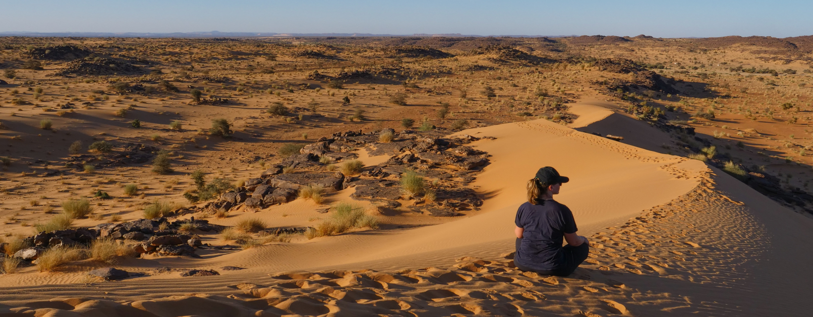 Une femme assise dans le sable regarde l'horizon désertique
