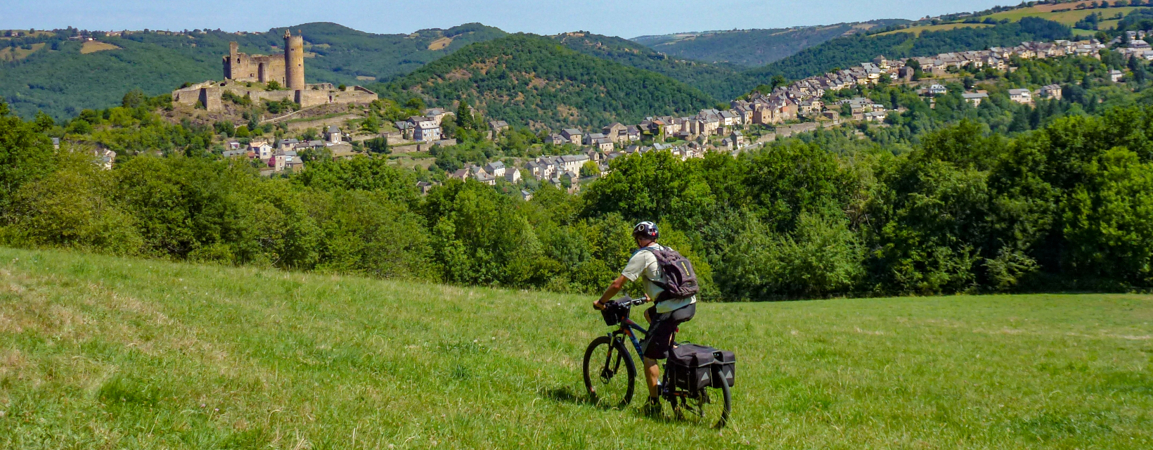 Un cycliste traverse un champ face à la bastide de Najac