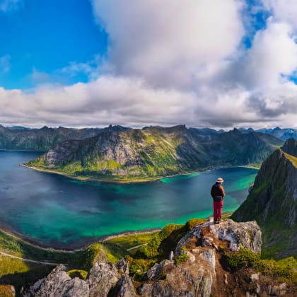 Randonneur debout au sommet du mont Husfjellet sur l'île de Senja, dans le nord de la Norvège, profitant d'une vue spectaculaire sur les fjords et les montagnes environnantes.