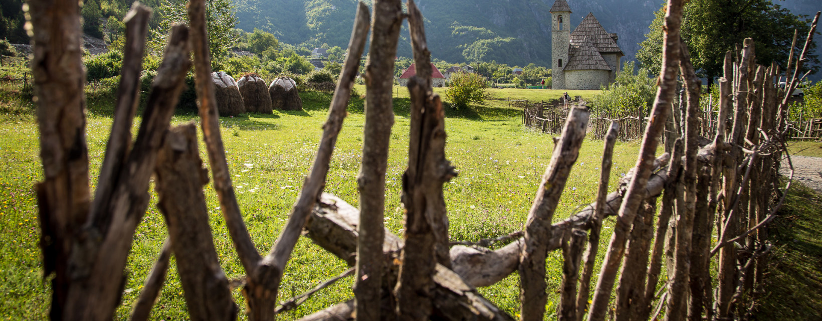 Vue d'une petite église entourée de montagnes verdoyantes en Albanie, avec une clôture rustique en bois au premier plan