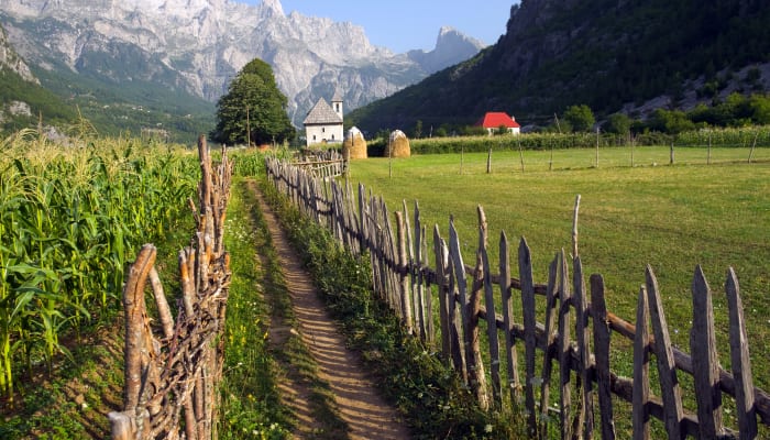 Un chemin au milieu des champs avec vue sur les montagnes de la vallée de Theth en Albanie